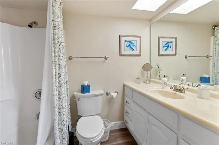 Bathroom featuring toilet, hardwood / wood-style flooring, a shower with curtain, vanity, and a skylight