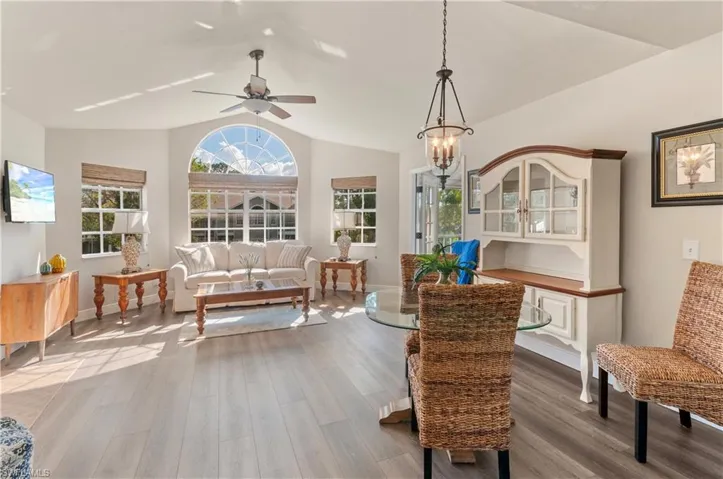 Living area featuring vaulted ceiling, ceiling fan with notable chandelier, and wood-type flooring