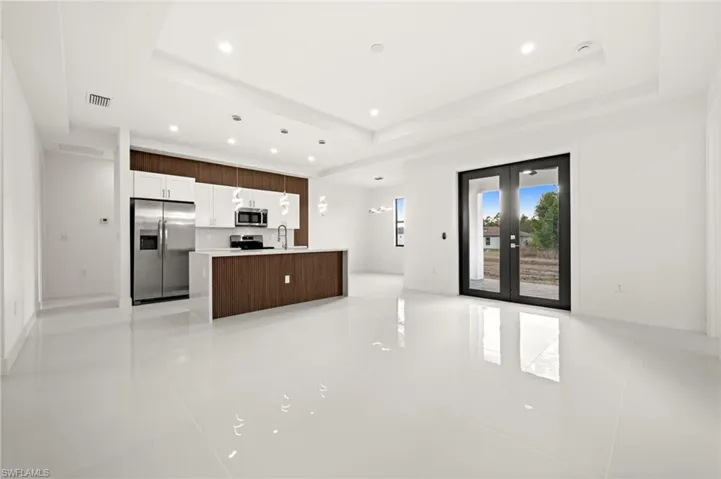 Kitchen featuring open floor plan, french doors, stainless steel appliances, a kitchen island with sink, and recessed lighting