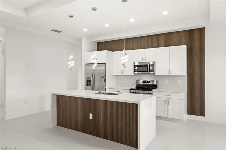 Kitchen featuring stainless steel appliances, light stone counters, pendant lighting, and white cabinetry