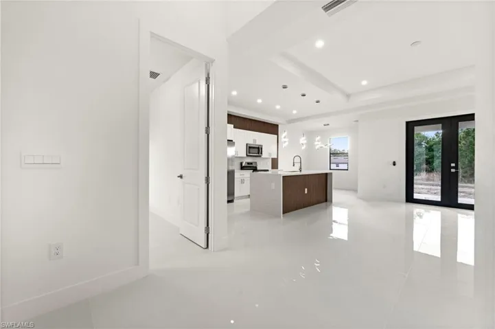 Kitchen with french doors, an island with sink, hanging light fixtures, white cabinetry, and open floor plan