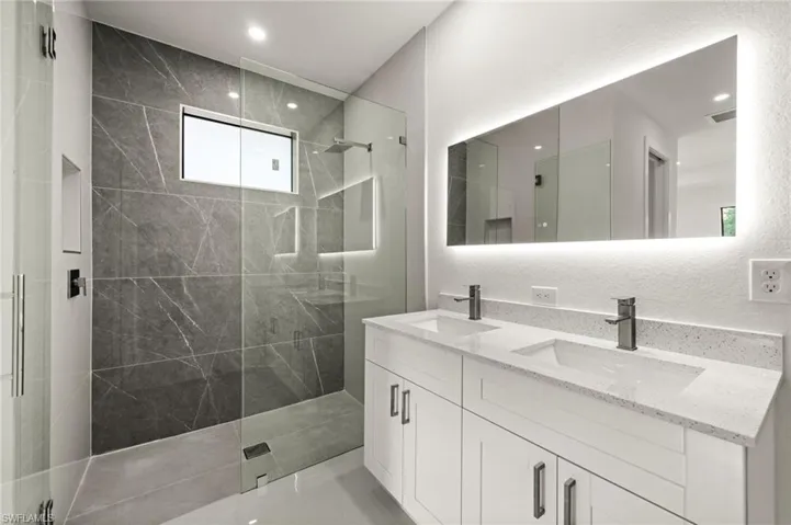 Full bathroom with a textured wall, double vanity, walk in shower, and recessed lighting