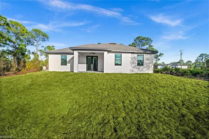 Rear view of property featuring stucco siding, a lawn, a patio area, and roof with shingles