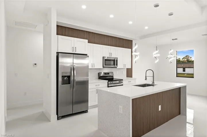 Kitchen with stainless steel appliances, pendant lighting, white cabinets, light stone countertops, and an island with sink