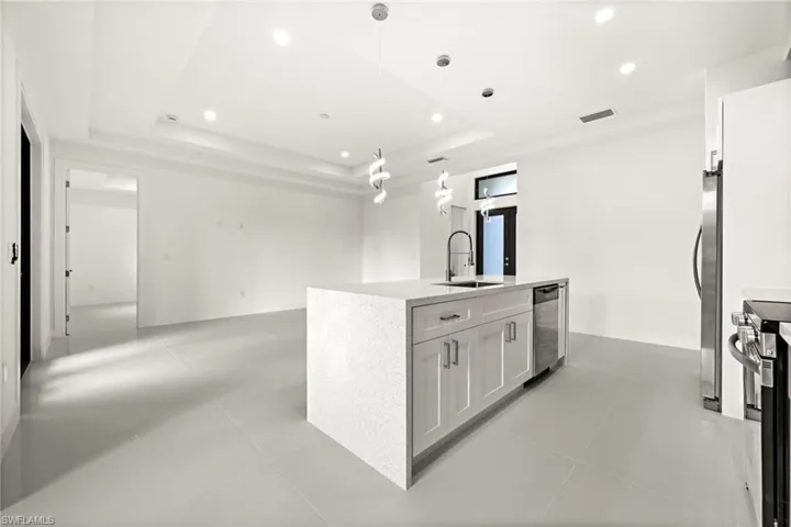 Kitchen with light stone countertops, white cabinets, hanging light fixtures, stainless steel appliances, and a tray ceiling