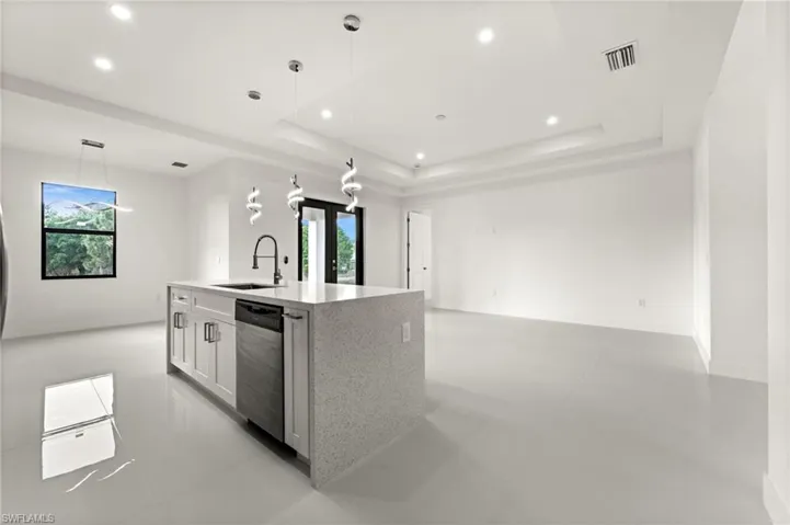 Kitchen with light stone countertops, decorative light fixtures, dishwasher, open floor plan, and white cabinetry