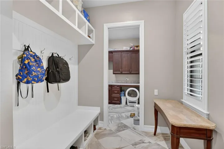 Built-in white storage bench with open cubbies and hanging hooks, complemented by an overhead shelf