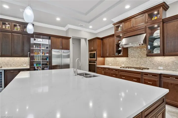 Spacious kitchen featuring a large central island with an integrated sink, rich wood cabinetry, stainless steel appliances, a tiled backsplash, and recessed lighting