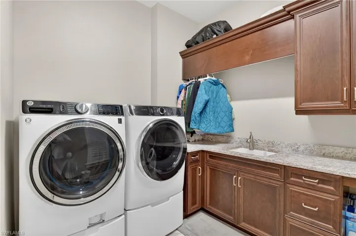 Dedicated laundry area featuring a built-in sink, stone-finish countertops, wood-finish cabinetry, and overhead storage