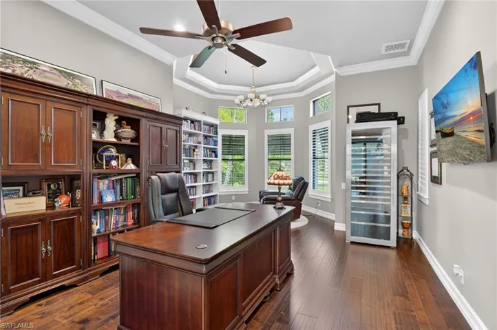 Expansive study featuring rich wood-finish flooring, built-in shelving, and a tray ceiling with a ceiling fan