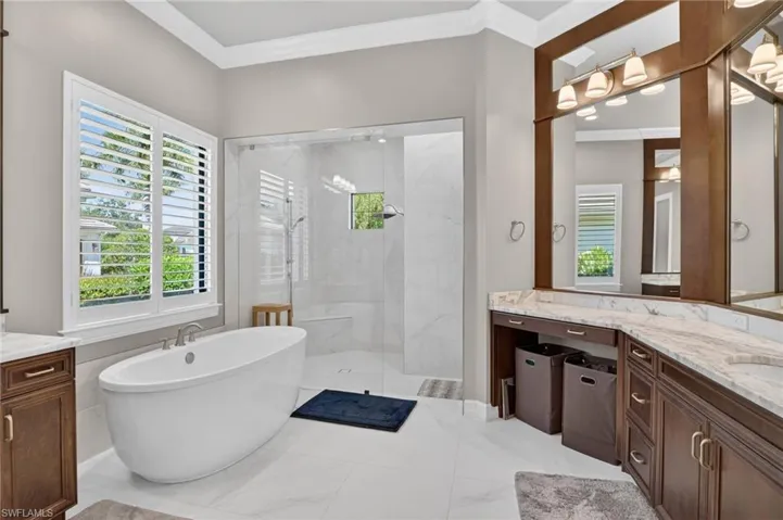 Bathroom with a freestanding soaking tub, an expansive walk-in shower with a built-in bench, dual vanity with undermount sinks and stone countertops, and plantation shutters