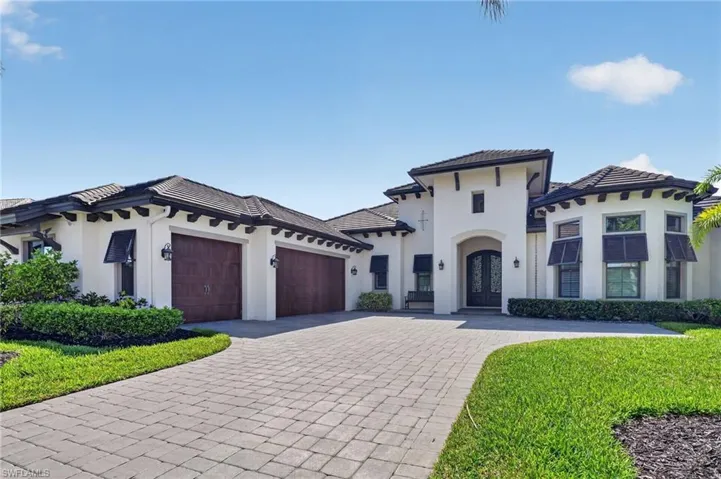 Luxury exterior with a tile roof, featuring a paver driveway, dark wood-finish garage doors, and a grand arched entry with double doors