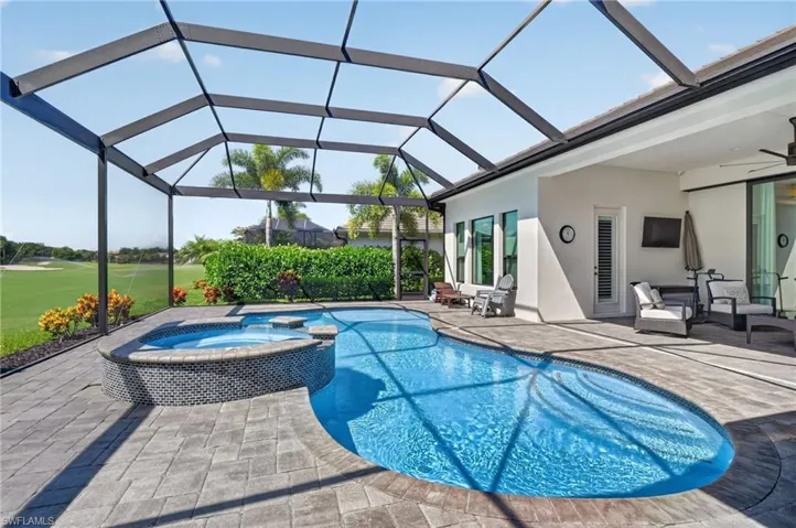 Screened-in outdoor living space featuring a freeform pool, integrated spa with mosaic tile, and paver decking