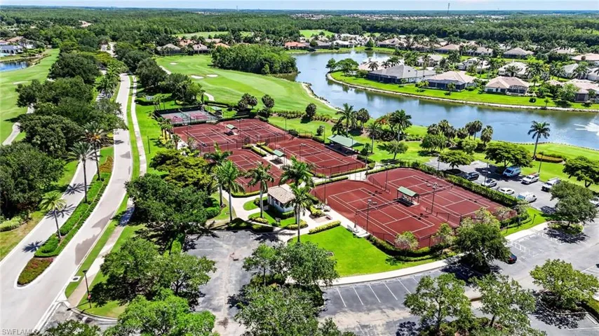 Expansive tennis court complex featuring multiple red clay courts, surrounded by manicured landscaping and palm trees