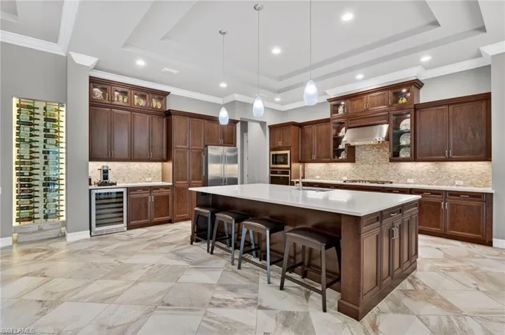 Gourmet kitchen featuring a large central island with seating, extensive dark wood cabinetry, an integrated wine storage display, stainless steel appliances, and large format tile flooring