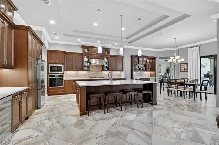 Gourmet kitchen with wood cabinetry, stainless steel appliances, a large central island with seating, and marble-pattern tile flooring
