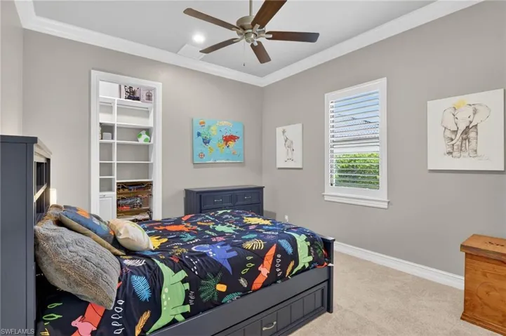Recessed built-in shelving, crown molding, a ceiling fan with light fixture, and plush carpet flooring define this room