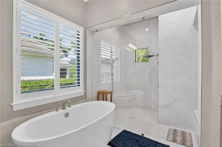 Freestanding soaking tub with brushed nickel fixtures, plantation shutters, and a frameless glass shower enclosure featuring a built-in bench and large format tile