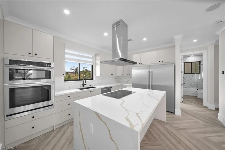 Kitchen with backsplash, appliances with stainless steel finishes, a sink, a kitchen island, and island range hood