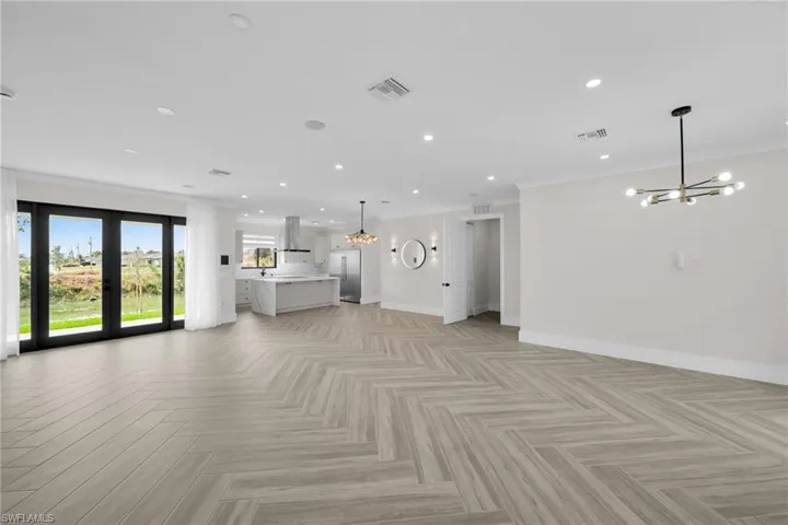 Unfurnished living room featuring baseboards, ornamental molding, visible vents, and an inviting chandelier
