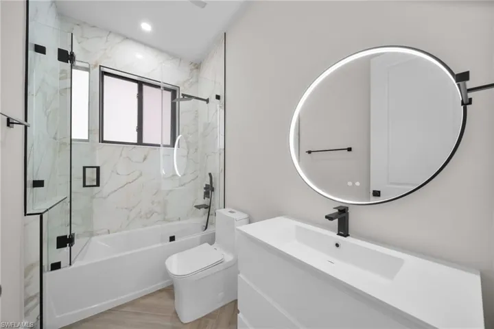 Bathroom with toilet, wood finished floors, combined bath / shower with glass door, vanity, and recessed lighting