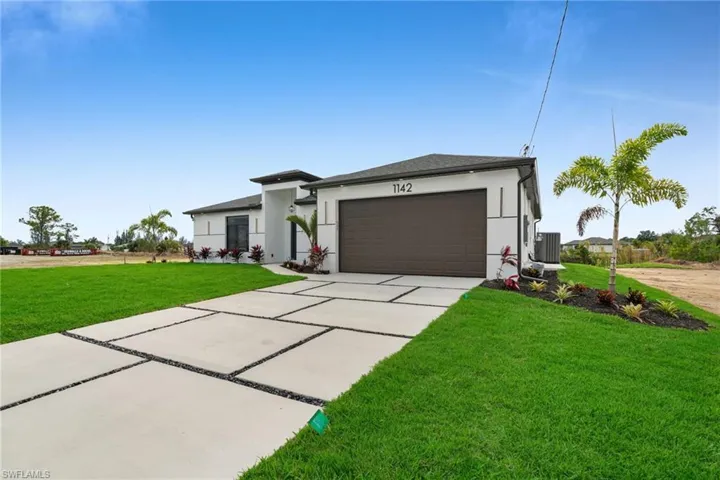 View of front of property with a garage, driveway, a front lawn, and stucco siding
