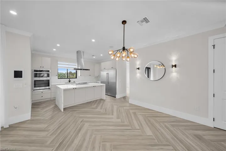 Kitchen with island exhaust hood, stainless steel appliances, light countertops, visible vents, and white cabinets