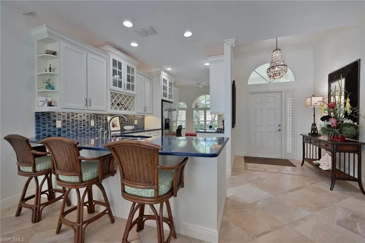 Kitchen with white cabinets, a kitchen breakfast bar, glass insert cabinets, decorative backsplash, and a peninsula