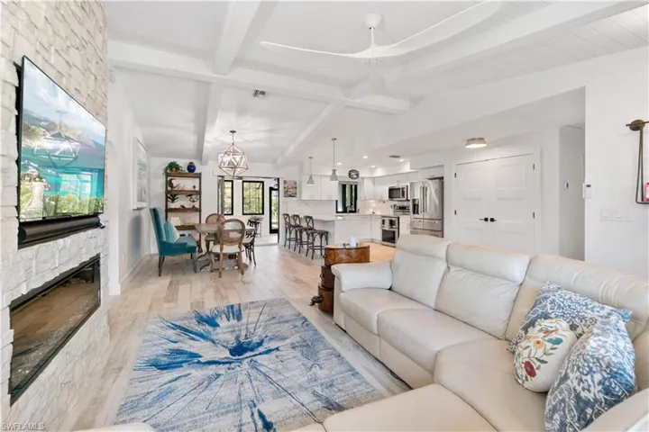 Living room featuring vaulted ceiling with beams, a notable chandelier, a fireplace, and light wood-type flooring