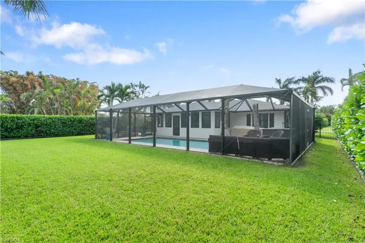 Back of house with a fenced in pool, a lanai, and a lawn
