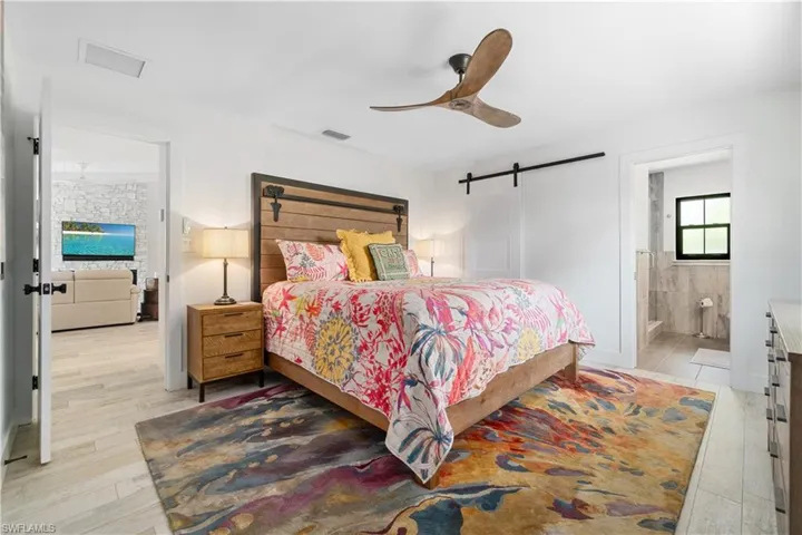 Bedroom featuring ensuite bathroom, a barn door, light wood-type flooring, and ceiling fan