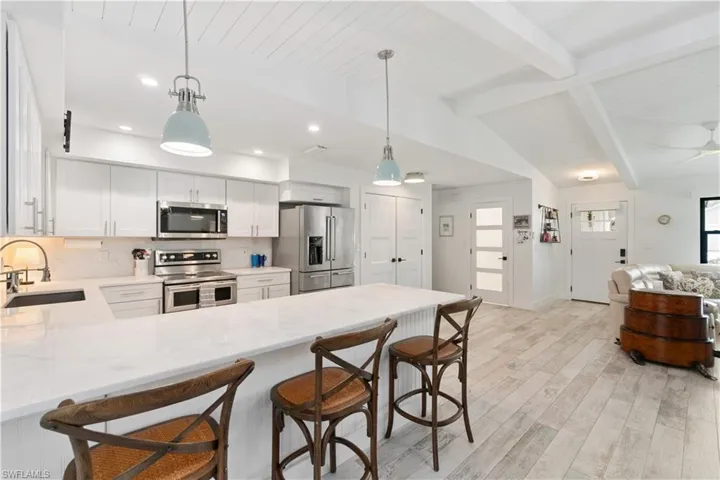 Kitchen featuring appliances with stainless steel finishes, sink, lofted ceiling with beams, hanging light fixtures, and light hardwood / wood-style floors