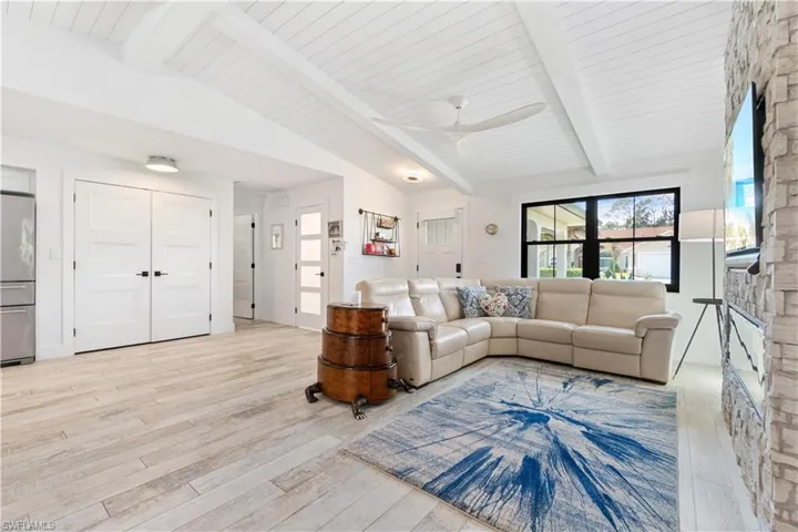 Living room featuring light hardwood / wood-style floors, lofted ceiling with beams, a fireplace, and ceiling fan