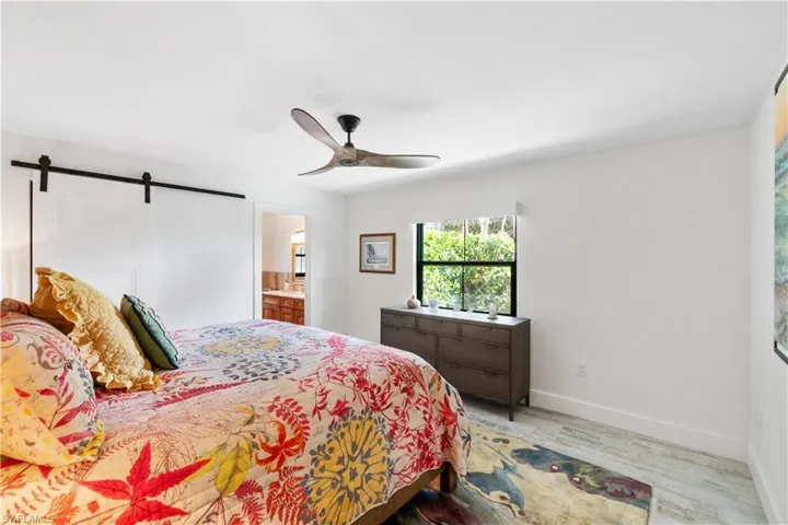 Bedroom featuring hardwood / wood-style floors, a barn door, ensuite bath, and ceiling fan