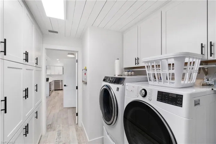 Clothes washing area with washing machine and dryer, light wood-type flooring, and cabinets