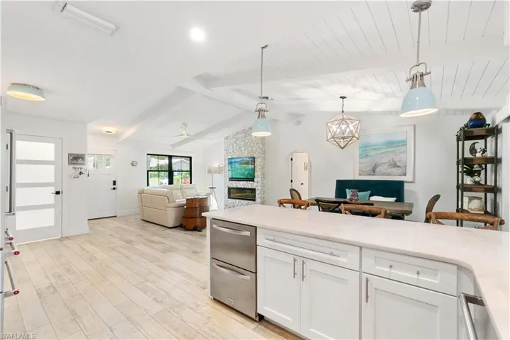 Kitchen featuring lofted ceiling with beams, a stone fireplace, hanging light fixtures, white cabinetry, and light hardwood / wood-style flooring