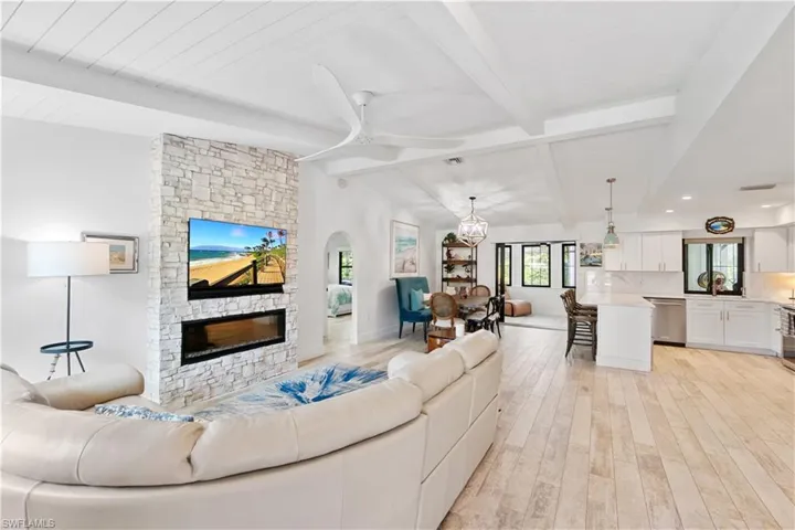 Living room featuring a fireplace, lofted ceiling with beams, light wood-type flooring, and ceiling fan