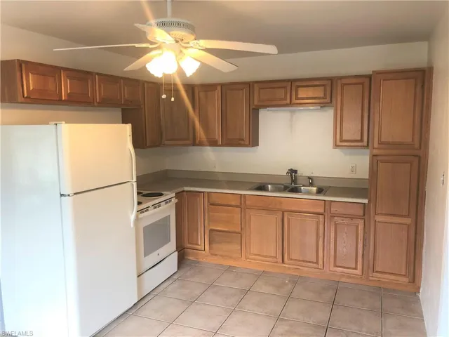 Kitchen with white appliances, ceiling fan, wood finish cabinetry, and light tile patterned floors