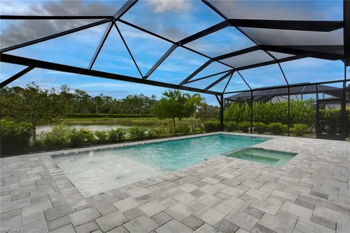 View of pool featuring a patio area, a water view, a pool with connected hot tub, and a lanai
