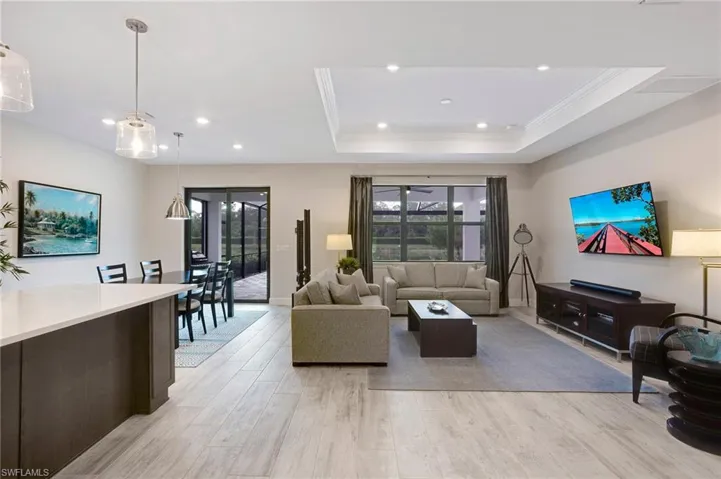 Living area with ornamental molding, plenty of natural light, light wood-style floors, recessed lighting, and a tray ceiling