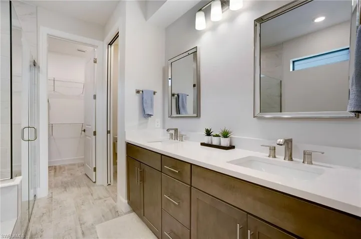 Full bathroom featuring double vanity, a shower stall, a walk in closet, and wood finished floors