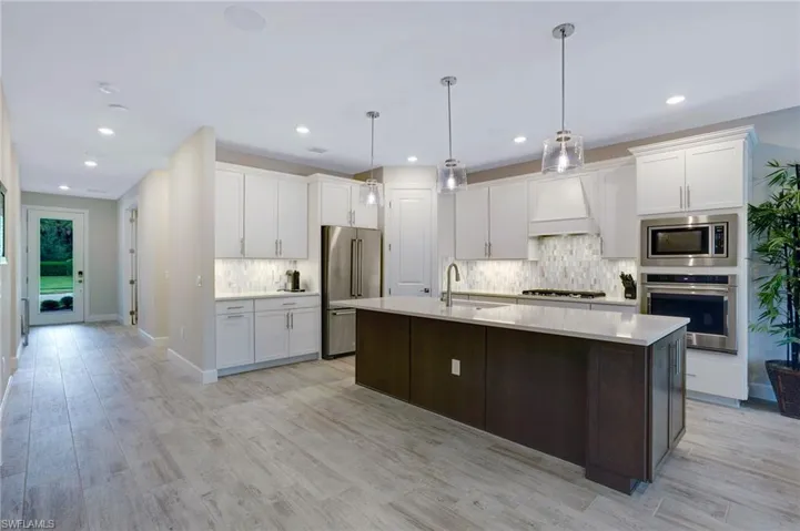 Kitchen with appliances with stainless steel finishes, custom range hood, tasteful backsplash, light countertops, and white cabinetry