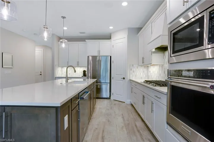 Kitchen with stainless steel appliances, light wood-type flooring, light countertops, white cabinets, and recessed lighting