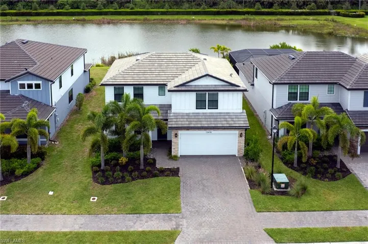 View of front of property with decorative driveway, a water view, an attached garage, board and batten siding, and a front lawn