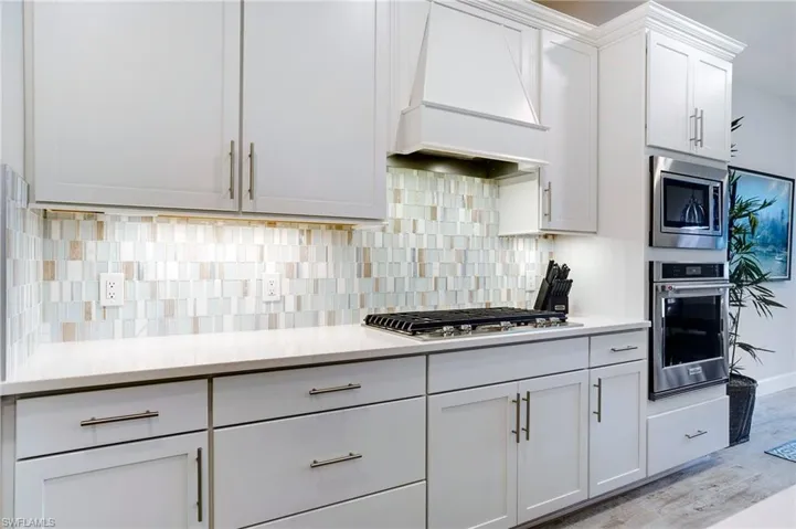 Kitchen featuring appliances with stainless steel finishes, premium range hood, light countertops, and white cabinetry