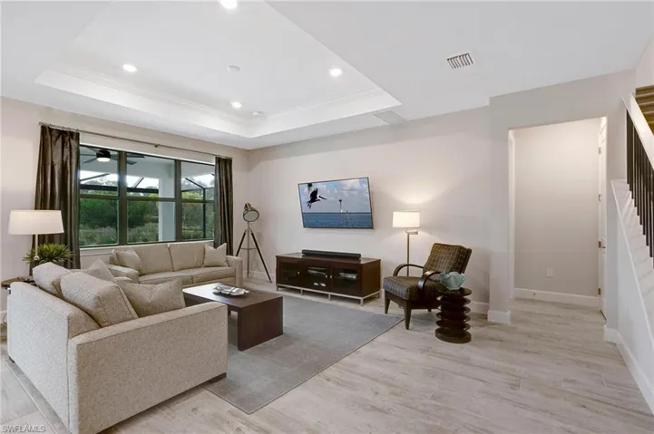 Living area featuring crown molding, light wood-style floors, a tray ceiling, recessed lighting, and stairs