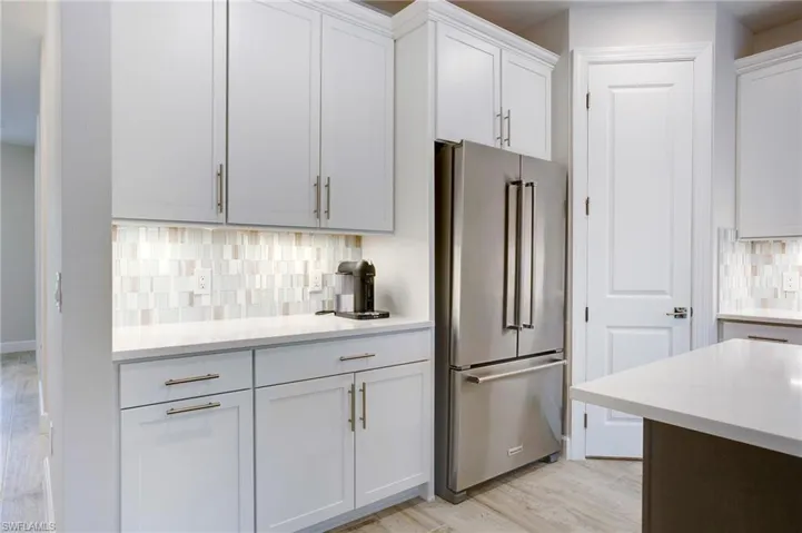 Kitchen with high end refrigerator, light countertops, decorative backsplash, white cabinets, and light wood-type flooring