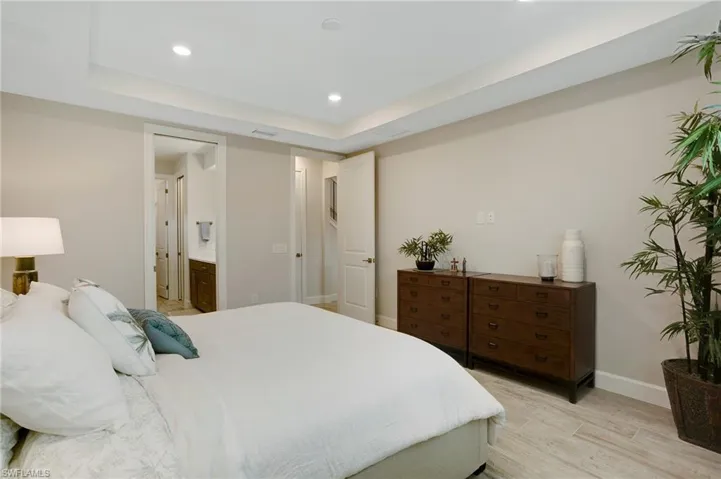 Bedroom featuring light wood finished floors, a raised ceiling, recessed lighting, and connected bathroom