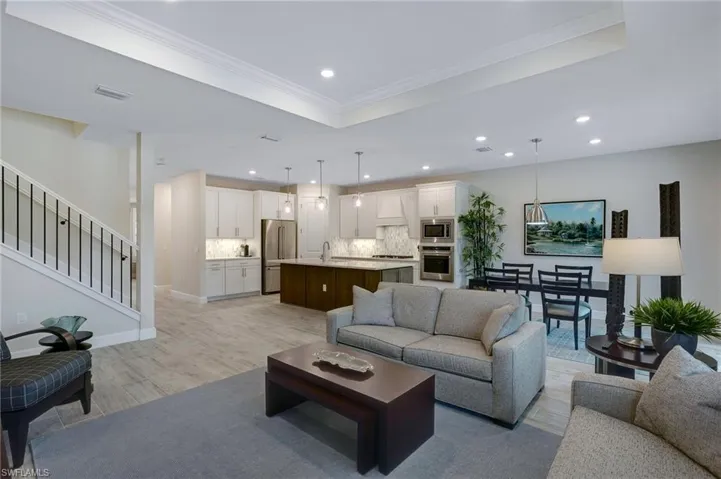 Living room with light wood finished floors, recessed lighting, crown molding, a raised ceiling, and stairs