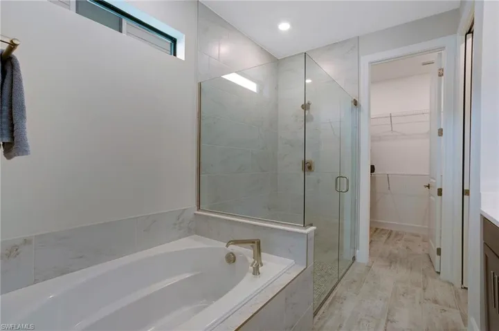 Full bathroom featuring a bath, a stall shower, a walk in closet, and vanity